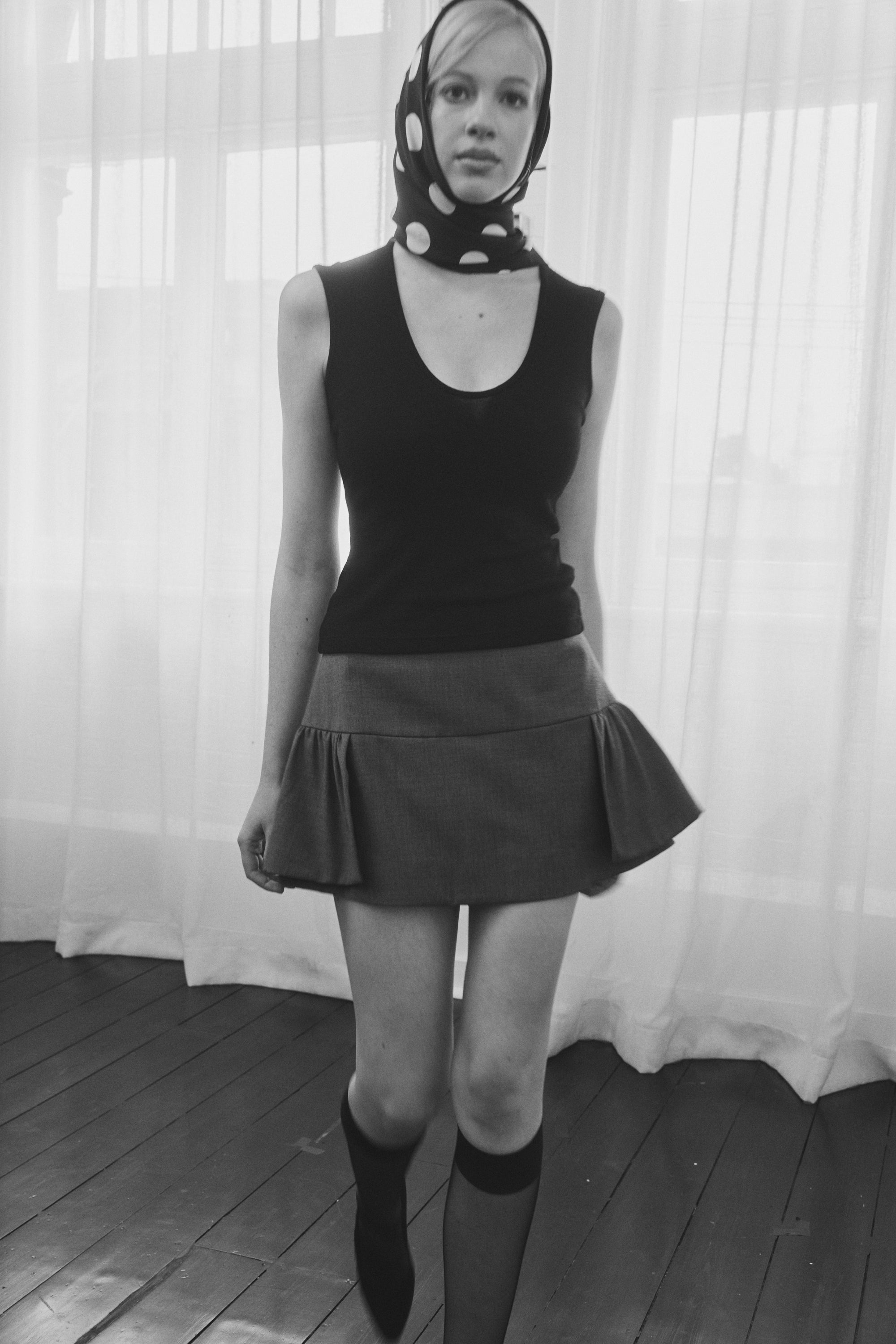 Woman wearing a black and white polka dot silk scarf by Australian label nessi, styled over the head against a soft white curtain backdrop.