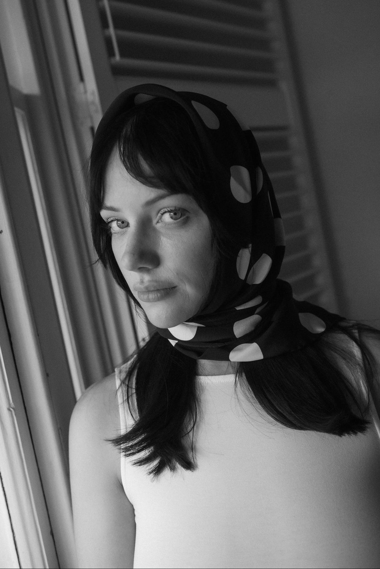 Woman wearing a black silk square scarf with white polka dots around the head, a handmade silk scarf by nessi, an Australian independent fashion label.