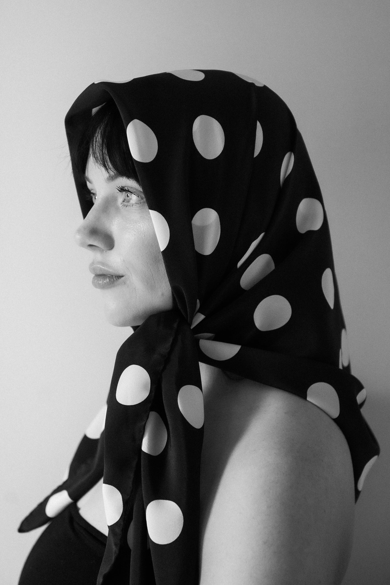 Woman wearing large square silk scarf by nessi tied around head, black with white polka dots, Australian independent fashion label.
