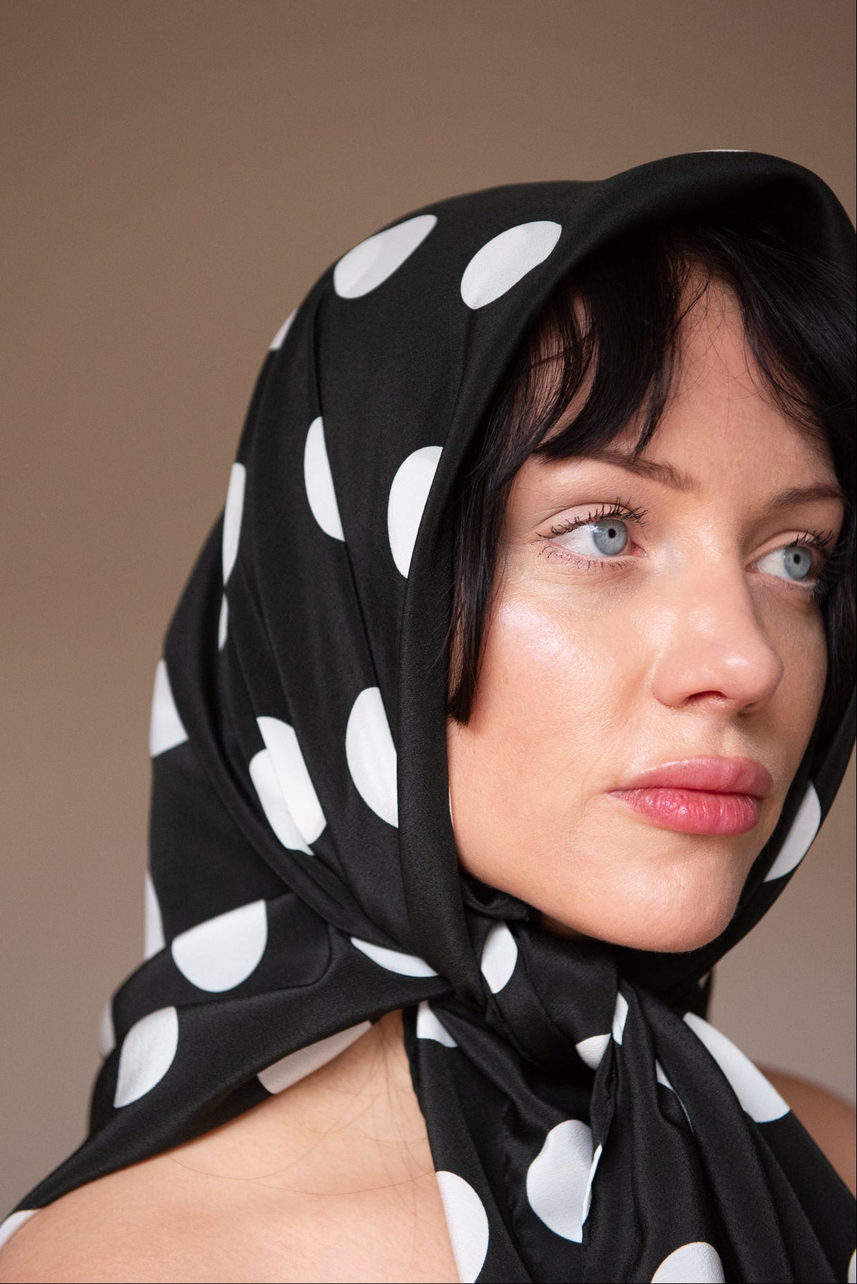 Woman wearing a black silk square scarf with white polka dots around the head, a handmade silk scarf by nessi, an Australian independent fashion label.