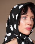 Woman wearing a black silk square scarf with white polka dots around the head, a handmade silk scarf by nessi, an Australian independent fashion label.